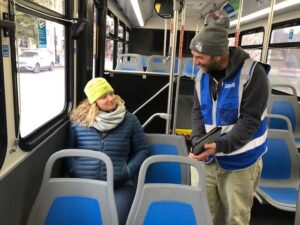 A man in a blue vest surveys a woman bus rider on the bus